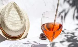 Ein Aperol Spritz im Glas neben einem Strohhut und einem Buch.
