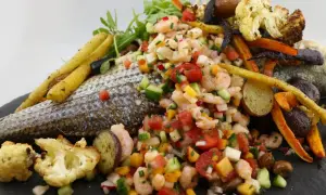 Poisson au barbecue avec salade de crevettes, légumes rôtis et herbes fraîches. Un plat coloré et savoureux.