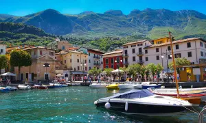 Barche ormeggiate nel porto di Salò, sul Lago di Garda, con case colorate e montagne verdi sullo sfondo.