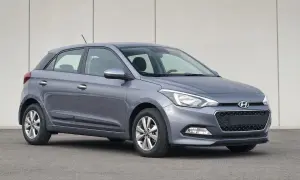Szary Hyundai i20 z włączonymi światłami pozycyjnymi na tle jasnej ściany.
