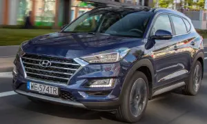 Nowy Hyundai Tucson w ciemnoniebieskim kolorze jedzie ulicą. Elegancki design i nowoczesne linie podkreślają jego dynamiczny charakter.