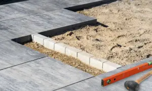 Układanie płyt betonowych na piasku, z widocznym krawężnikiem i narzędziami budowlanymi.