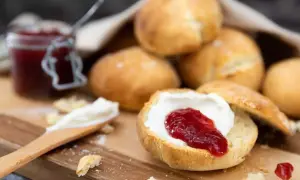 Lyxiga scones med grädde och sylt på en träbricka. En härlig fika!