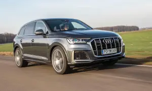 Szary Audi Q7 z napędem quattro pędzi po drodze, mijając zielone pola.