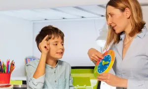 Bambino impara a leggere l'ora con una terapista occupazionale che usa un orologio colorato.
