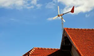 Małe wiatraki energetyczne na dachu domu, obracające się na tle błękitnego nieba z chmurami.