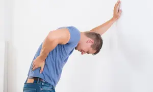 Uomo con mal di schiena appoggiato al muro, cerca rimedi naturali per il mal di schiena.