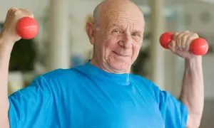 Ein lächelnder älterer Mann macht Muskeltraining im Alter mit roten Hanteln.