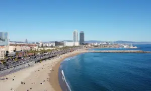 Słoneczna plaża Barceloneta z turkusową wodą, palmami i nowoczesnymi budynkami w tle.