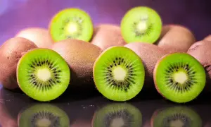 Kilka przekrojonych i całych kiwi na ciemnym tle z fioletowym rozmyciem w tle.