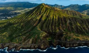 Widok z lotu ptaka na zielone wzgórza i ocean, gdzie leży Honolulu. W oddali widać zabudowania.