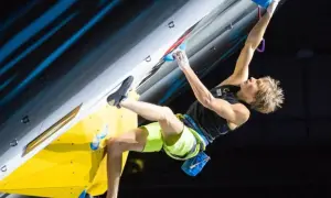 Alex Megos kämpft sich an einer Kletterwand hoch, seine Muskeln angespannt.