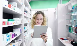 Farmacéutica sonriente revisa inventario en su tablet, rodeada de estantes llenos de productos de atida mifarma.