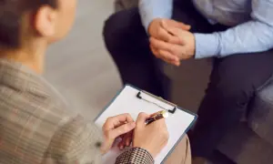 Sesja terapeutyczna, gdzie psychoterapeuta notuje ważne informacje. To obraz postępu w kierunku regulacji zawodu, jak ustawa o zawodzie psychoterapeuty.