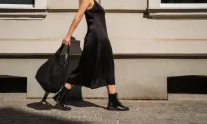 Kobieta w czarnej sukience i czarnych rajstopach idzie ulicą, niosąc torbę. Idealne buty do czarnych rajstop to te, które widzisz na jej stopach.
