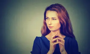 Kobieta z podejrzanym wyrazem twarzy i splecionymi palcami. Może to symbolizować rozważania nad przyczynami osobowości paranoicznej.