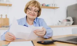 Starsza pani z okularami przegląda dokumenty. Może to rachunki z rp-7 zlikwidowanego zakładu pracy.