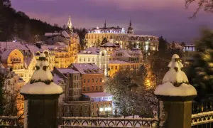 Winterliche Pracht in Karlsbad: verschneite Gebäude unter violettem Abendhimmel, beleuchtet von warmem Licht.
