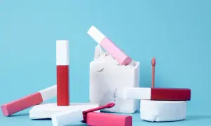 Różowe i czerwone błyszczyki do ust, niektóre z białymi nakrętkami, leżą na białych blokach. Ich formuła zawiera dwutlenek tytanu dla krycia.
