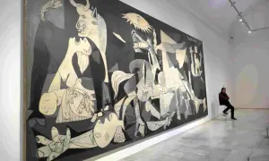 Pablo Picasso najsłynniejsze obrazy: "Guernica" w muzeum, z człowiekiem siedzącym na krześle i kontemplującym dzieło.