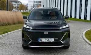 Czarny Geely Coolray z brązowym wnętrzem zaparkowany przed nowoczesnym budynkiem.