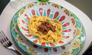 Pyszne tagliatelle al ragu podane w kolorowej miseczce z motywem kwiatowym. Obok leży widelec.