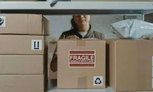 Pakowacz ręczny, kod zawodu 432301, przygotowuje paczki do wysyłki. Na zdjęciu widać stosy kartonów, jeden z napisem "FRAGILE".