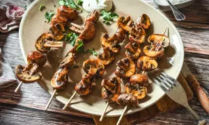 Gegrillte Champignons auf Spießen, garniert mit Kräutern und einem Klecks Dip. Perfekt für ein sommerliches BBQ.