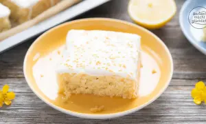 Ein Stück saftiger, veganer Zitronenkuchen mit weißer Glasur und goldenen Streuseln auf einem gelben Teller.