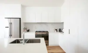 Cocinas modernas blancas con electrodomésticos de acero inoxidable, encimera de cuarzo y suelo de madera.