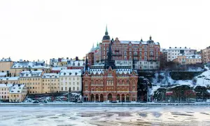 Vinter i Stockholm. Snöklädda byggnader längs vattnet, med en isig yta framför.