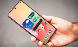 Main d'homme tenant un smartphone rouge, affichant des widgets météo et des icônes d'applications, dont Samsung Internet.