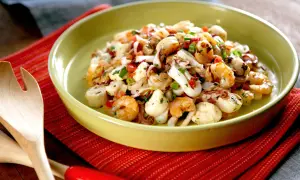 Deliciosa ensalada de marisco con camarones, calamares y vieiras, aderezada con hierbas frescas y pimientos.