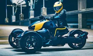 Kierowca w żółtym kasku na futurystycznym motorze trójkołowym Can-Am, gotowy do jazdy.