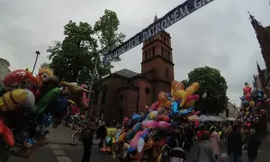 Kolorowe balony z postaciami z bajek i zwierzątkami, idealne gniezno atrakcje dla dzieci, na tle ceglanej wieży kościelnej i tłumu ludzi.