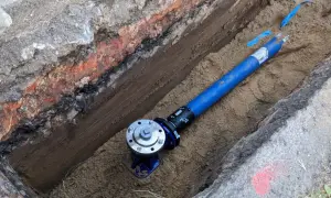 Blaues Rohr mit Ventil in einem ausgehobenen Graben.