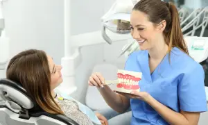 Uśmiechnięta higienistka stomatologiczna pokazuje pacjentce, jak prawidłowo szczotkować zęby na modelu szczęki.