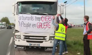 Des routiers accrochent une banderole sur un camion : "Carburants trop CHERS, Peuple en GALERE". Ils expriment leur mécontentement face au prix du carburant.