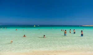 Ludzie kąpią się w krystalicznie czystej wodzie na plaży Makronissos. Słońce świeci, a niebo jest bezchmurne.