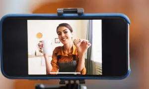 Frau hält Tasse und Keks, während sie ihr **iPhone als Webcam** für ein Kochvideo nutzt.