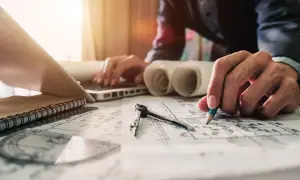 Rysowanie planów budowlanych, przygotowanie cennika usług budowlanych. Na stole leżą szkice, cyrkiel, laptop i notatnik.