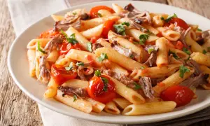 Penne z wieprzowiną i pomidorkami koktajlowymi, posypane natką pietruszki. Pyszne danie na obiad.