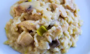 Un crémeux risotto poulet aux champignons et poireaux, servi sur une assiette blanche. Un plat réconfortant et savoureux.