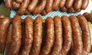 Prawdziwa wiejska kiełbasa przepis: świeżo uwędzone, rumiane kiełbaski wiszą na drewnianych kijach, gotowe do spożycia.