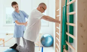 Fizjoterapeutka pomaga pacjentowi ćwiczyć na piłce rehabilitacyjnej przy drabinkach.