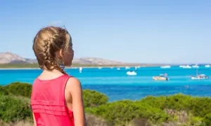 Dziewczynka z warkoczem podziwia turkusowe morze i łodzie. Wakacje we Włoszech z dziećmi to marzenie!