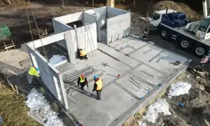 Budowa domu z keramzytu. Widać elementy prefabrykowane, dźwig i pracowników. Wady budowy mogą wynikać z trudnych warunków pogodowych, jak śnieg na placu budowy.