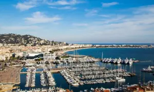 Widok na port w Cannes, gdzie cumują luksusowe jachty. W tle rozciąga się plaża i wzgórza. Idealne miejsce, by zobaczyć Cannes.
