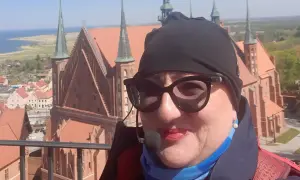 Kobieta w okularach i czapce na tle Fromborka. Wspaniałe widoki, idealne na rodzinne wycieczki i atrakcje dla dzieci.