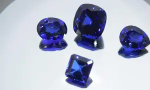 Cinco gemas de tanzanita piedra, de cortes y tamaños variados, brillan con un intenso color azul sobre un fondo reflectante.